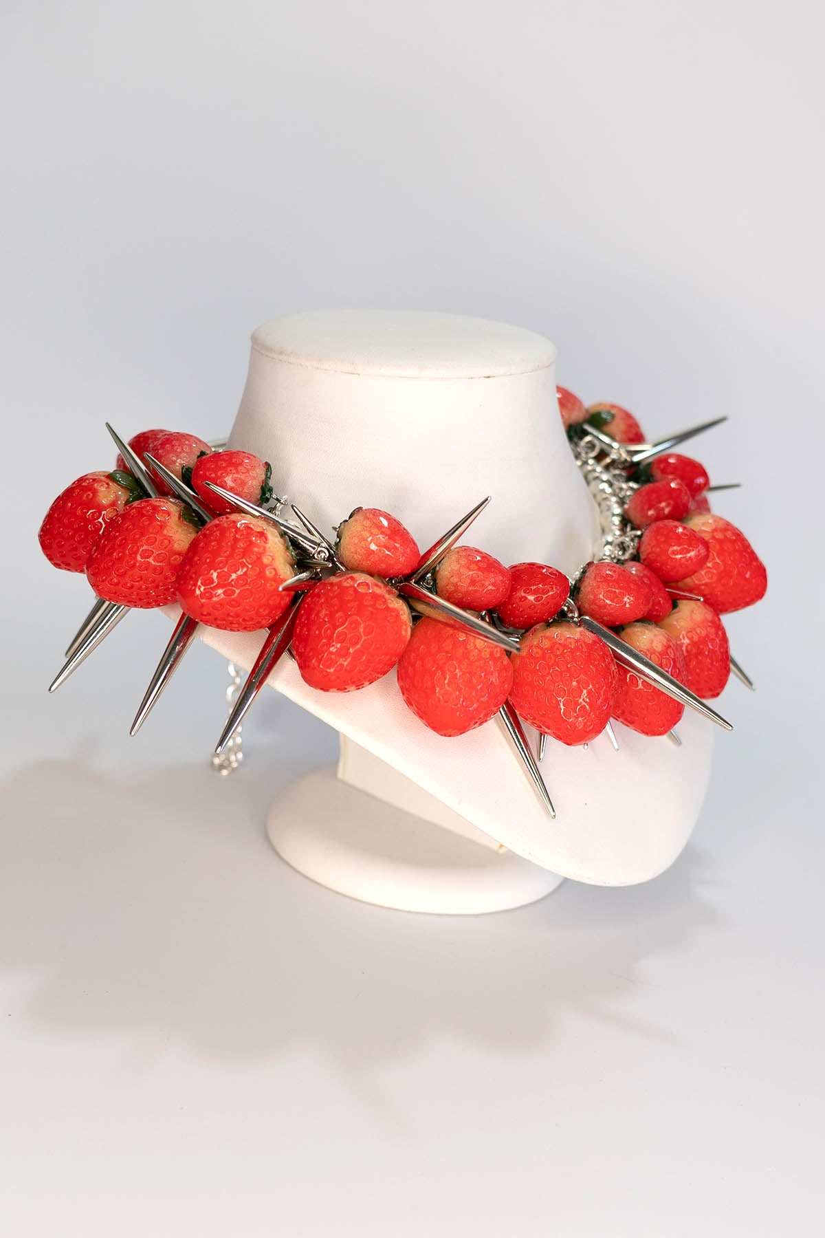 Necklace with red berries and spikes on a white mannequin head against a white background