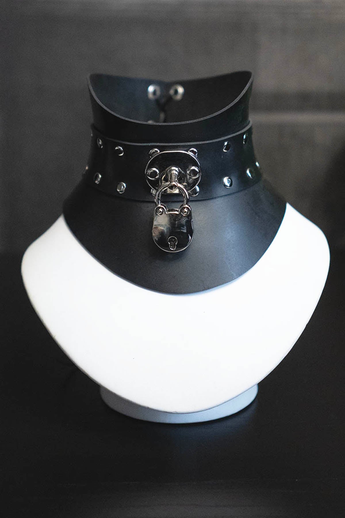 Black rubber choker with metal padlock on a white mannequin neck against a dark background
