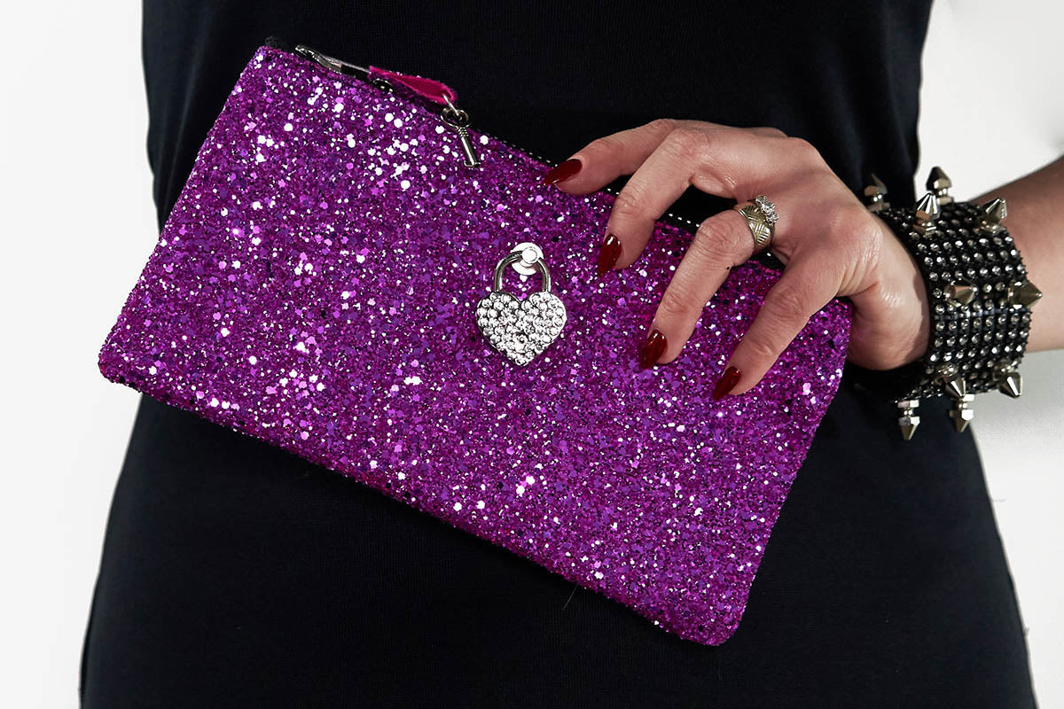 Bright Pink glittery clutch bag with a heart charm held by a person wearing a black outfit.