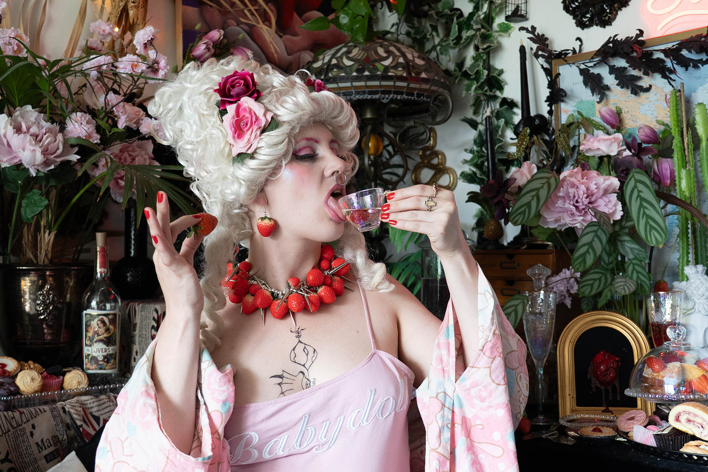 Woman in decorative outfit drinking from a small cup in a lushly decorated room.