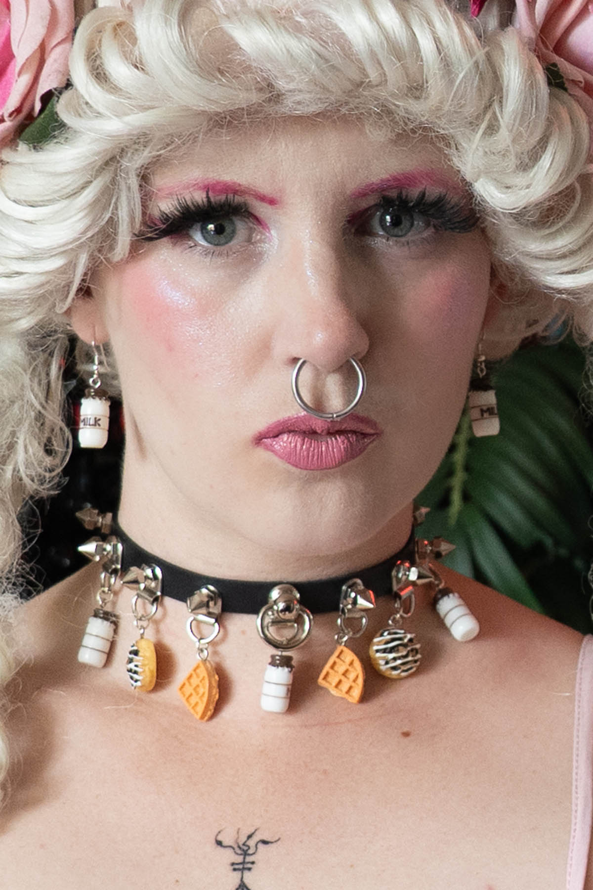 Person wearing a unique necklace with decorative pendants, surrounded by flowers.