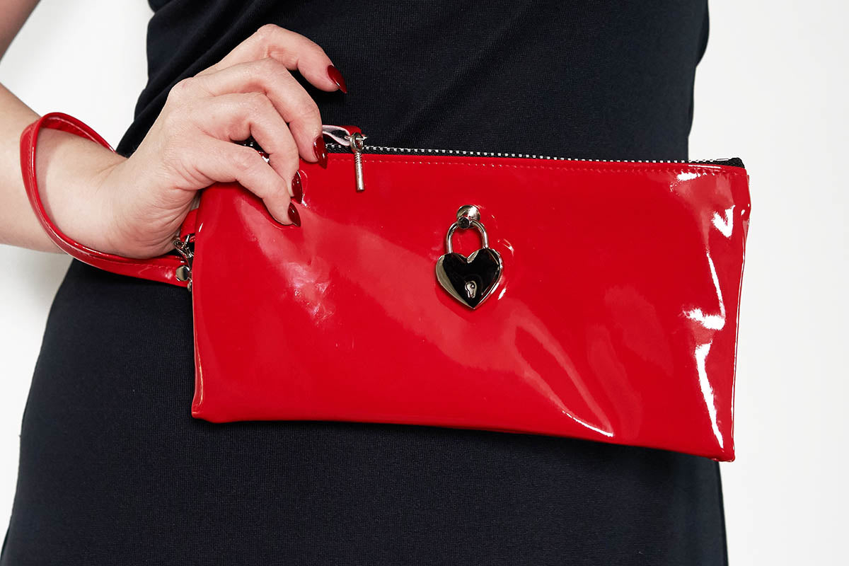Red clutch bag with a heart-shaped clasp held by a person wearing a black dress.