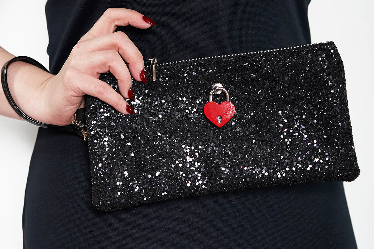 A black glittery clutch bag with a red padlock and a silver zipper, held in a person's hand.