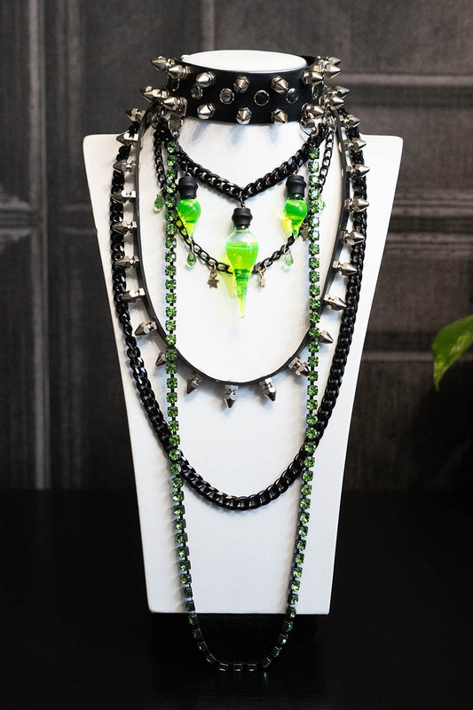 A display of layered chokers with black chains, spikes, and green crystal accents on a mannequin.