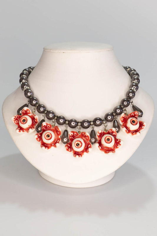 Necklace with red and black decorative pearls and eyeballs on a mannequin bust against a gray background