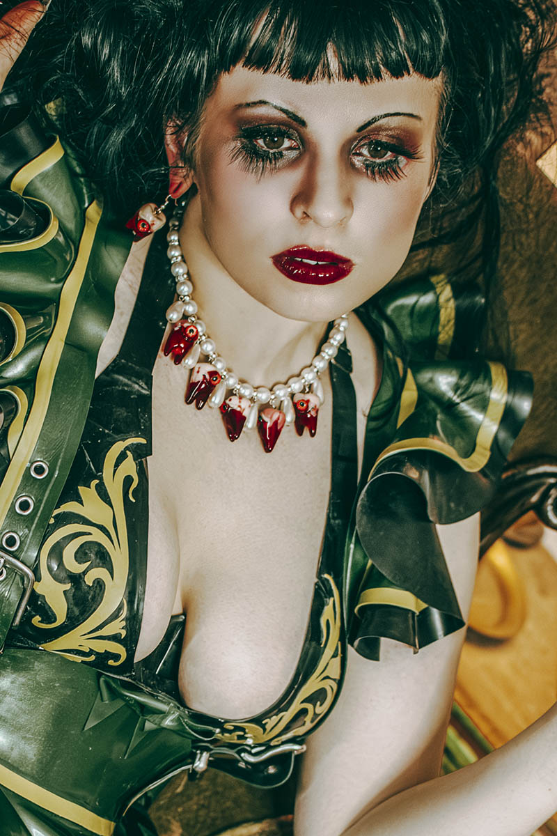 Woman in a green and gold costume with red jewelry against a blurred background