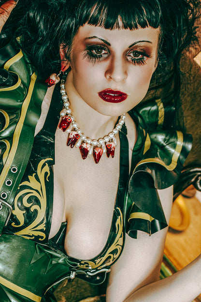 Woman in a green and gold costume with red jewelry against a blurred background