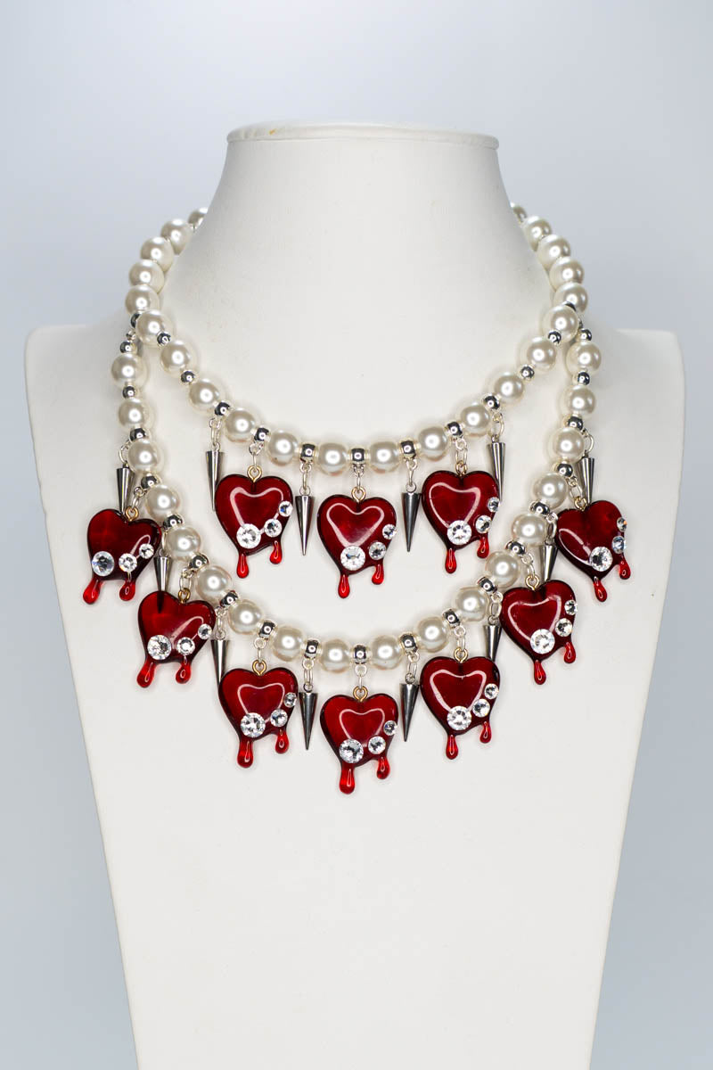 Necklace with red heart-shaped pendants and pearl-like beads on a mannequin.