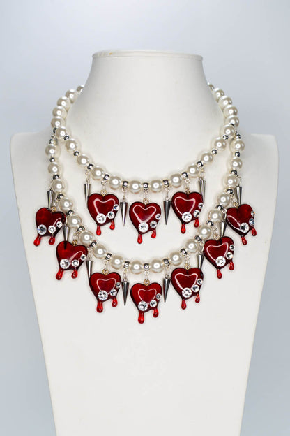 Necklace with red heart-shaped pendants and pearl-like beads on a mannequin.