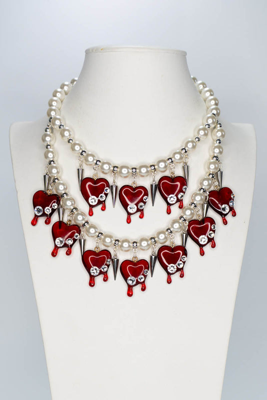 Necklace with red heart-shaped pendants and pearl-like beads on a mannequin.