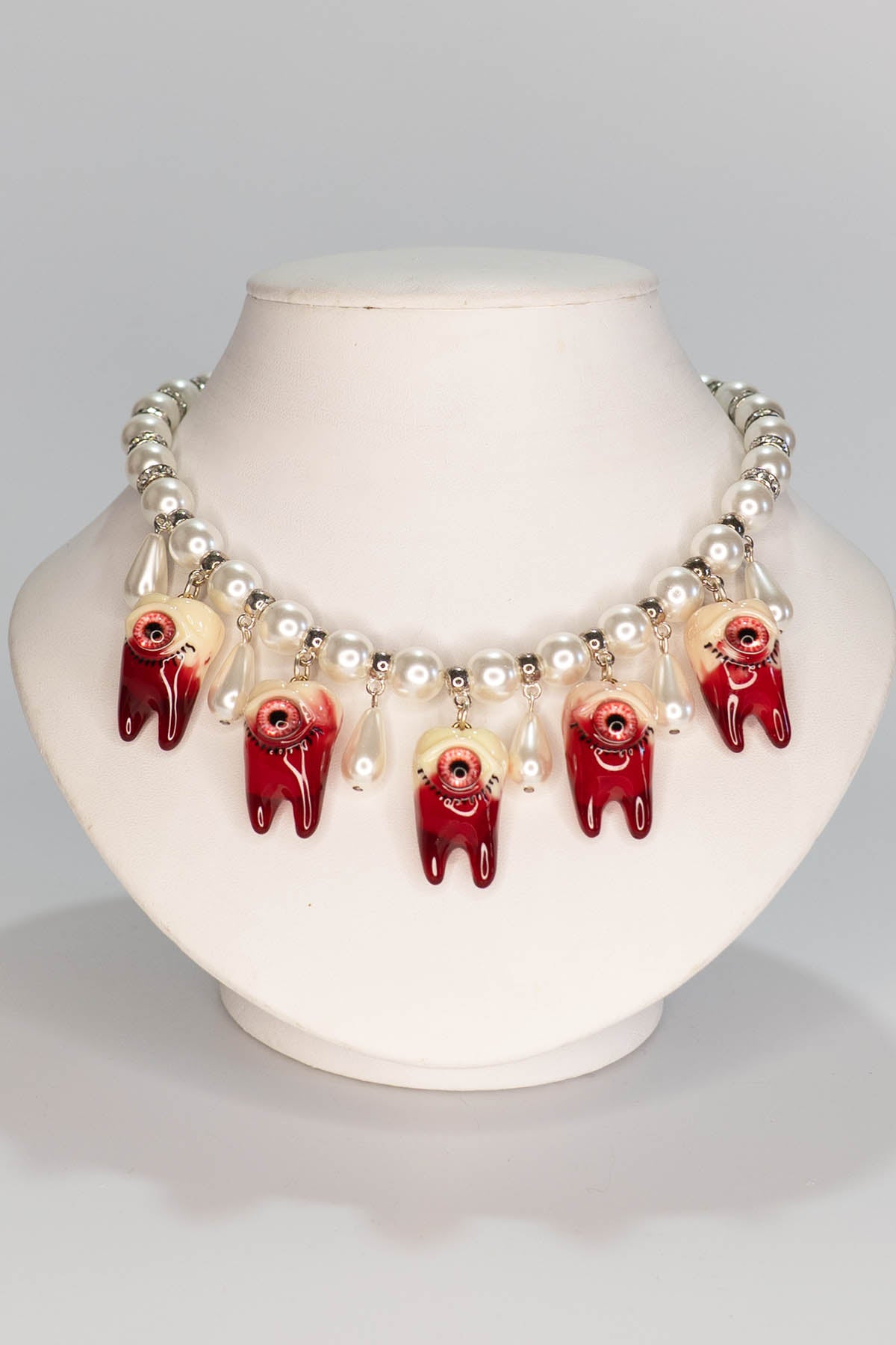 Necklace with red and white tooth beads on a mannequin bust against a gray background