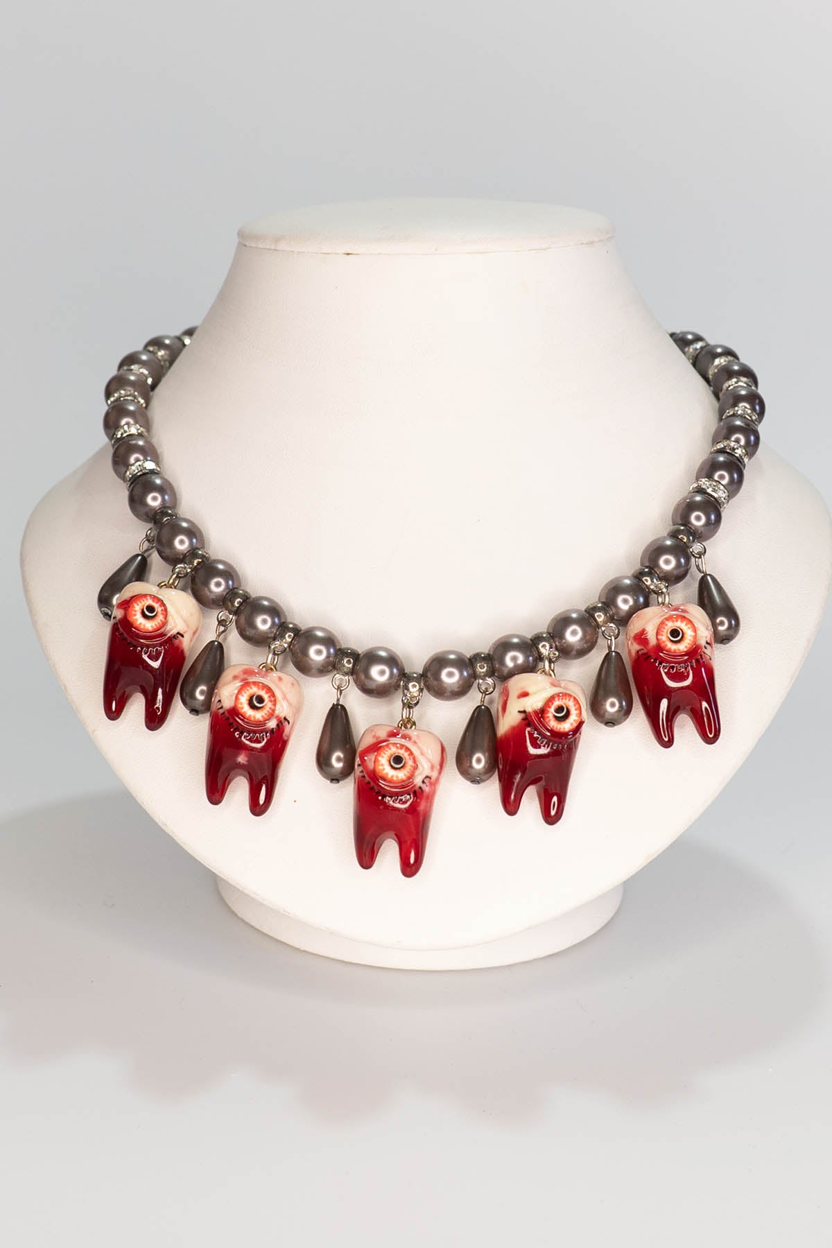 Necklace with red and black pearl beads on a mannequin bust against a gray background