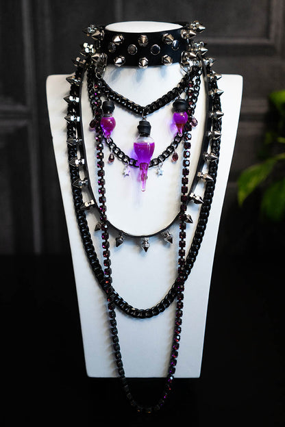 A black choker necklace with purple crystals, spikes, and a glass vial containing a purple liquid, displayed on a mannequin.