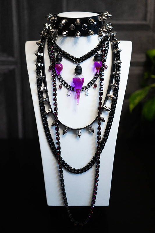 A black choker necklace with purple crystals, spikes, and a glass vial containing a purple liquid, displayed on a mannequin.