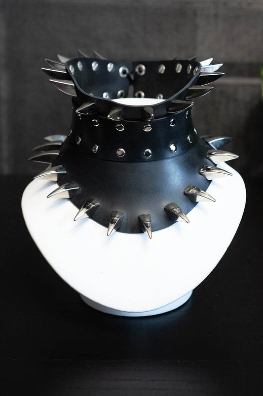 Black spiked collar on a white stand against a dark background