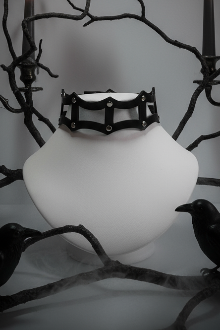 Black bracelet on a white vase with candles and crows in a dark setting