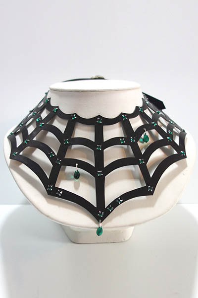 Black spider web necklace with green crystals on a white stand against a white background