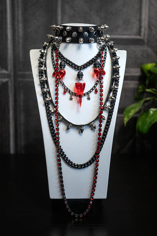 A layered-style choker necklace with black chains, red Preciosa crystals, and a glass bottle with red liquid, displayed on a mannequin.
