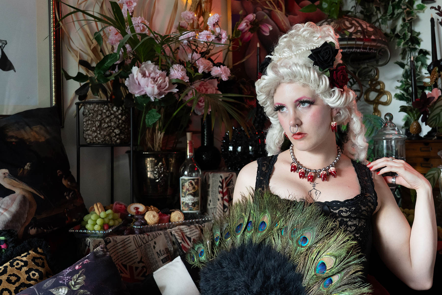 Woman in historical renaissance costume with peacock feather fan in a decorative setting.