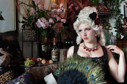 Woman in historical renaissance costume with peacock feather fan in a decorative setting.