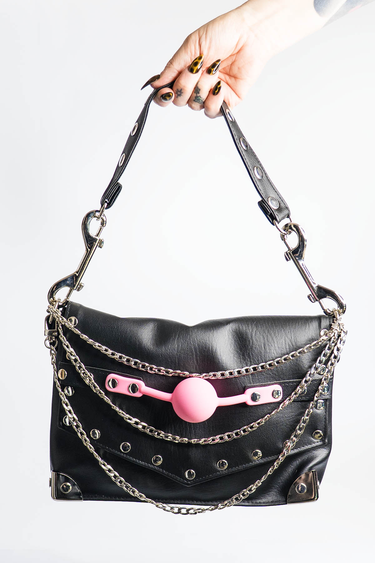 Black handbag with pink ball and chains held by a hand on a white background