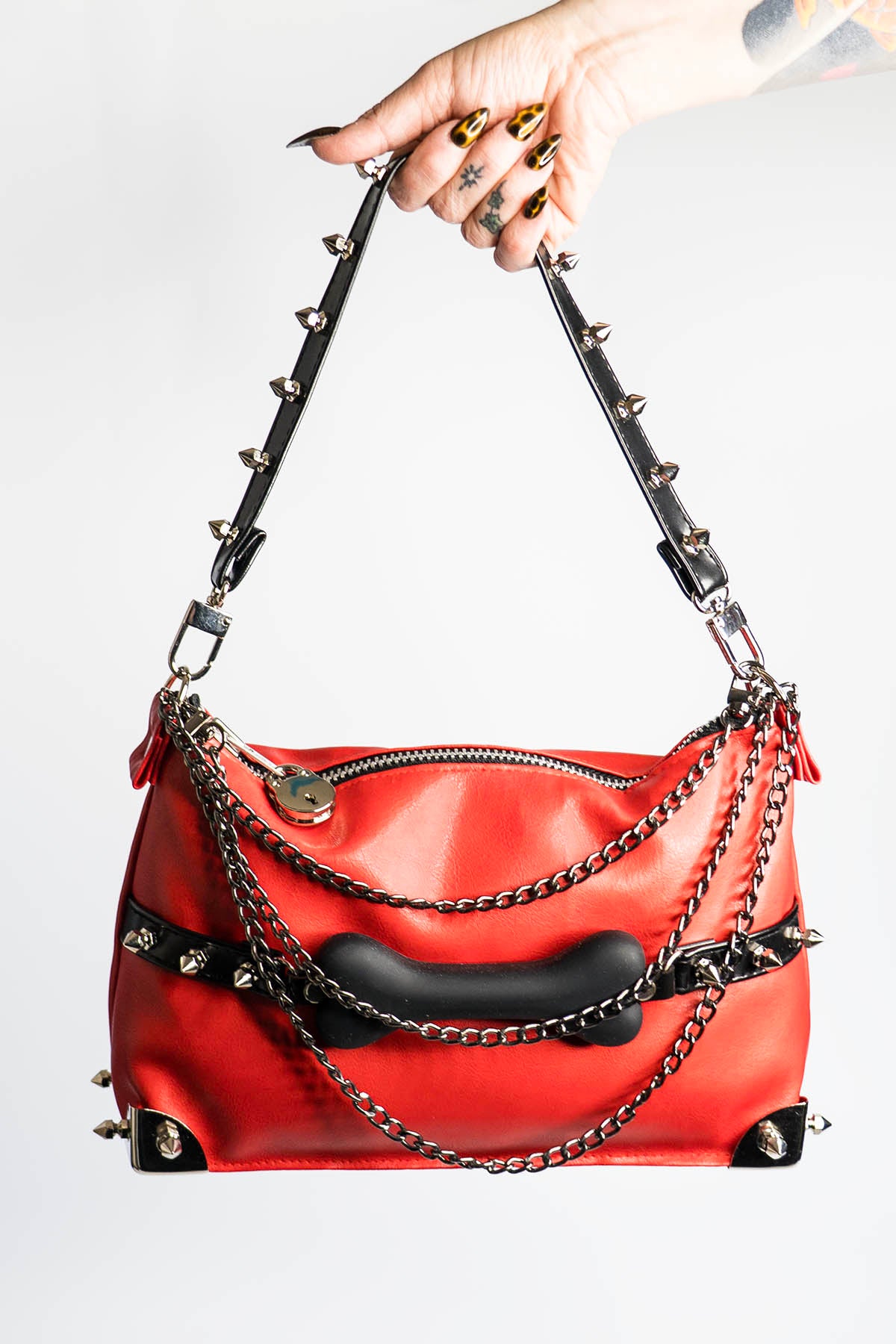 Red handbag with black accents and chain details held by a hand against a white background