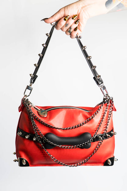 Red handbag with black accents and chain details held by a hand against a white background