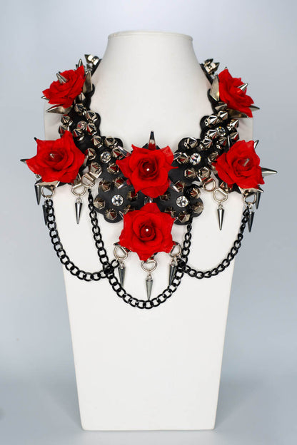 Necklace with red roses and spikes on a white stand against a light gray background