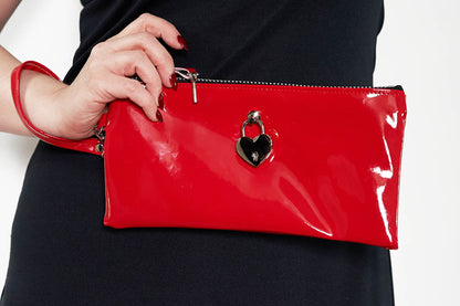 Red clutch bag with a heart-shaped clasp held by a person wearing a black dress.