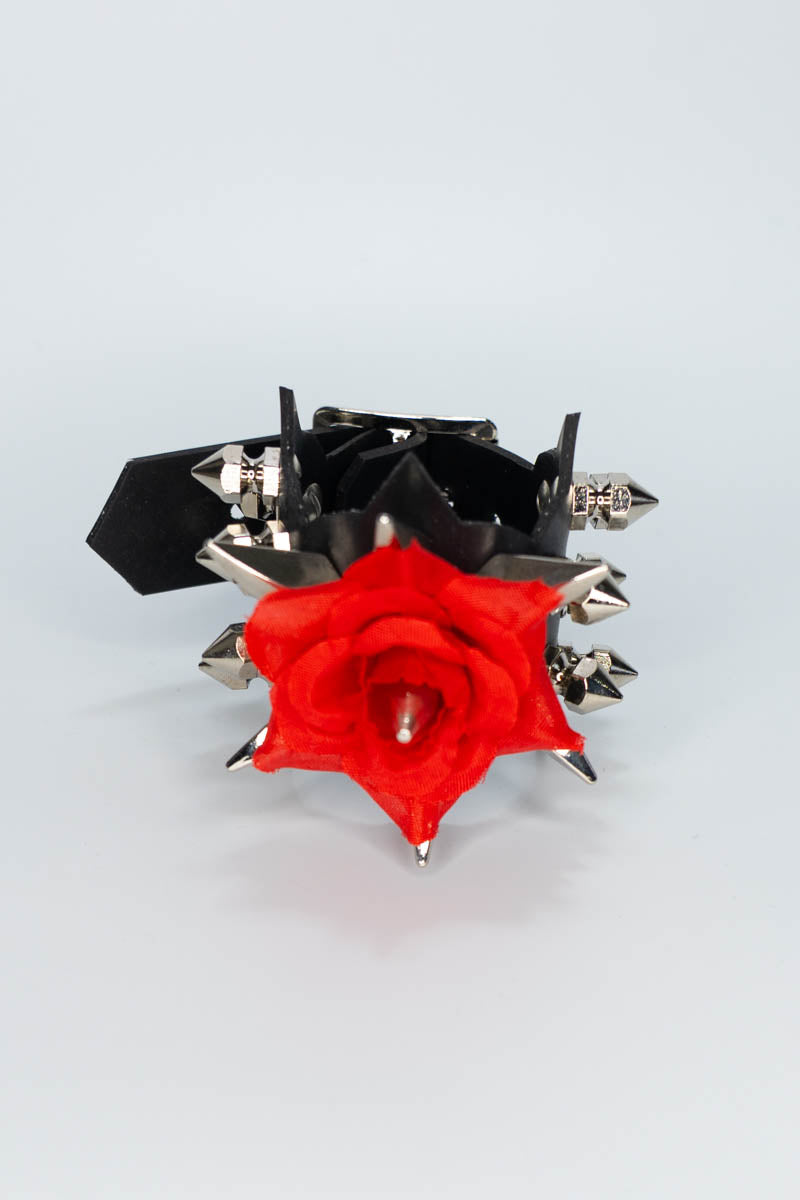 Black and silver spiked bracelet with a red rose on a light gray background