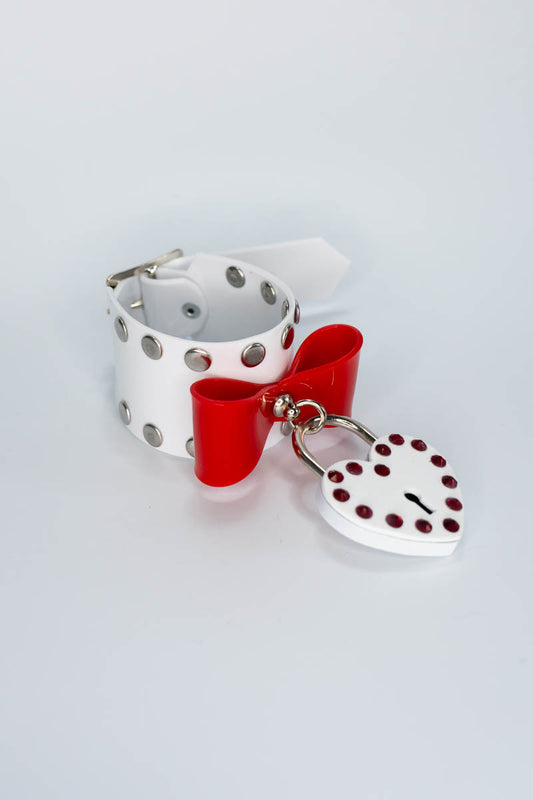 White pvc bracelet with red bow and heart-shaped tag on a light gray background