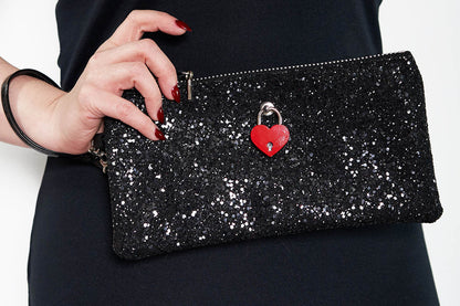 A black glittery clutch bag with a red padlock and a silver zipper, held in a person's hand.