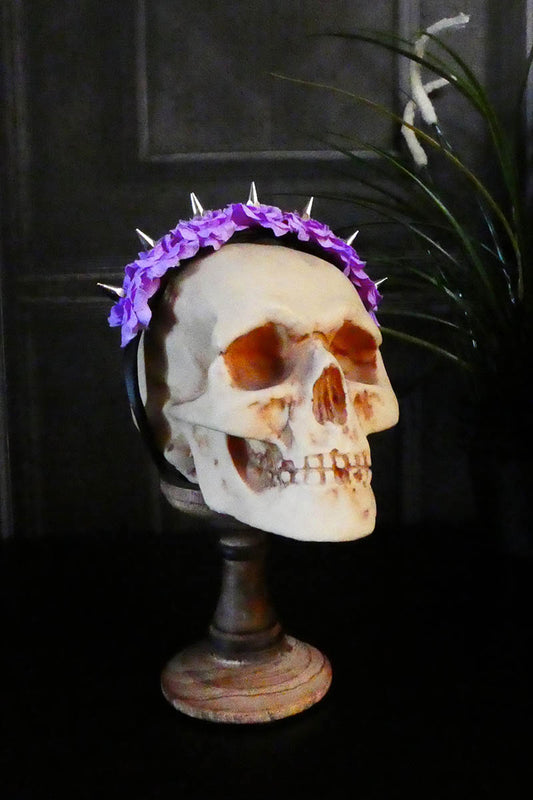 A white skull-shaped hairband adorned with purple silk roses and sharp spikes.